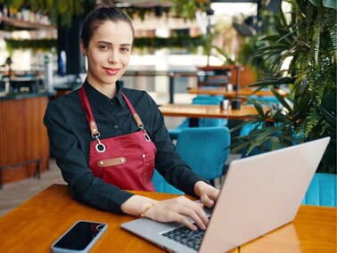 Restaurant owner managing social media marketing on a laptop inside their restaurant