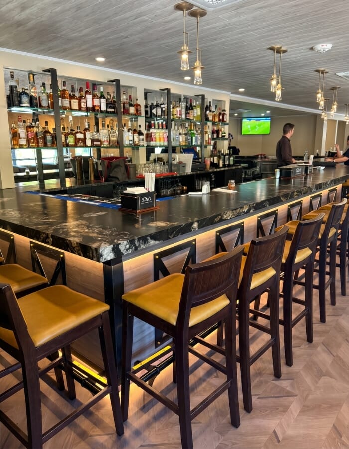 Renovated dining room with saffron upholstered restaurant chairs, gray tufted booths, black table tops, gold table bases, and warm pendant lights.