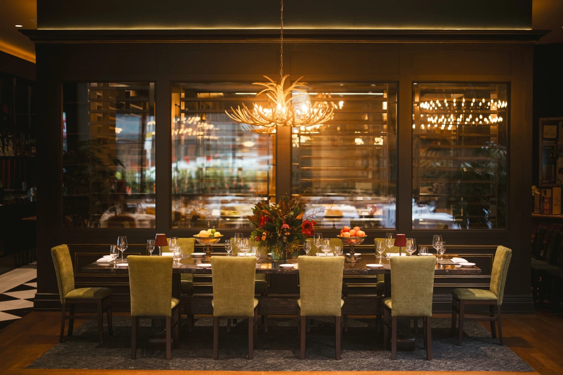 Communal dining table with upholstered chairs and chandelier lighting.