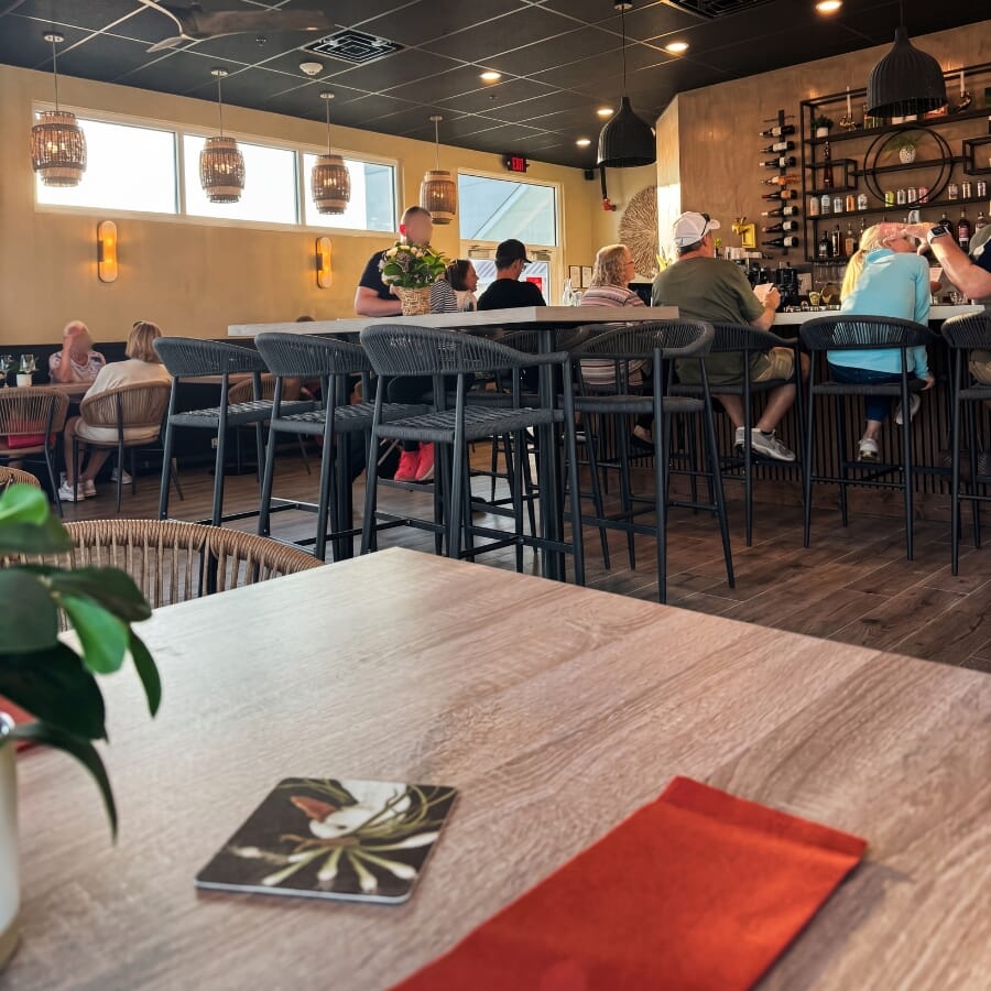 Wine bar seating area with gray restaurant bar stools, oak table surfaces, black commercial bases, and coastal neutral finishes.