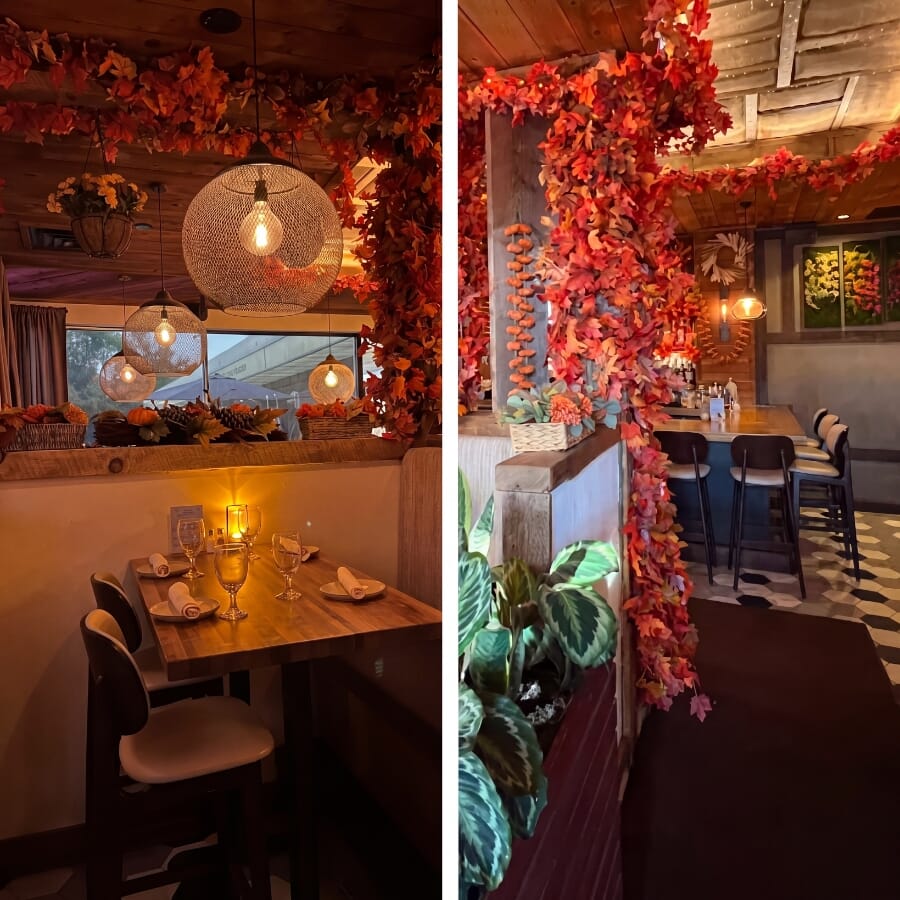 Bora Restaurant interior with floral ceiling installation, brick wall, fireplace, warm wood tables, and cream dining chairs.