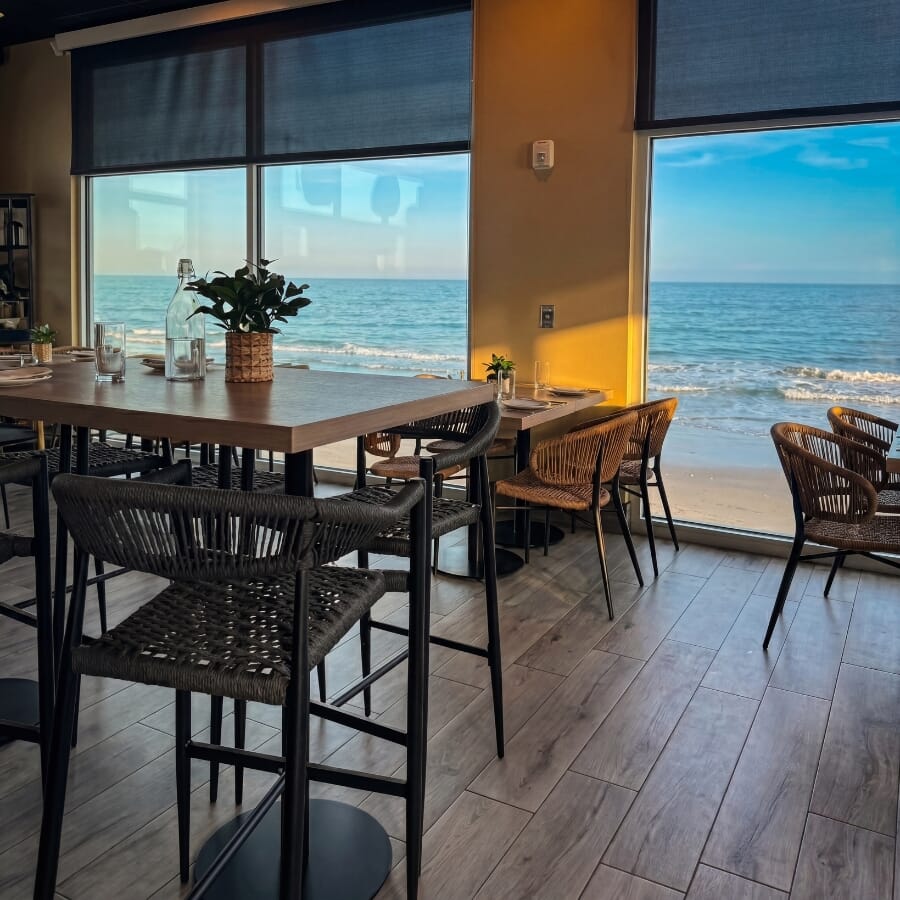 Restaurant seating layout featuring oak table tops, black powder coated table bases, tan rope dining chairs, and upholstered booth seating.