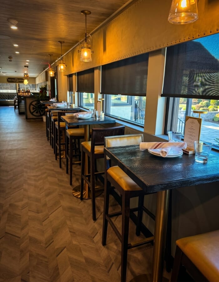 Restaurant dining room with black reclaimed ash table tops, gold table bases, saffron upholstered chairs, claret tufted booth seating, and warm lighting.
