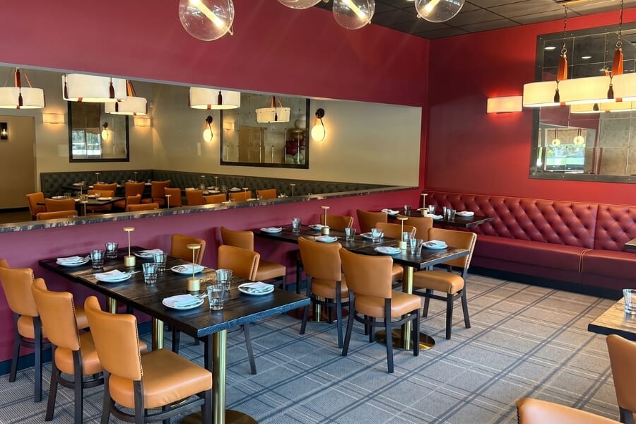 Renovated restaurant bar with Madison bar stools, walnut frames, saffron upholstery, black bar top, and warm lighting.
