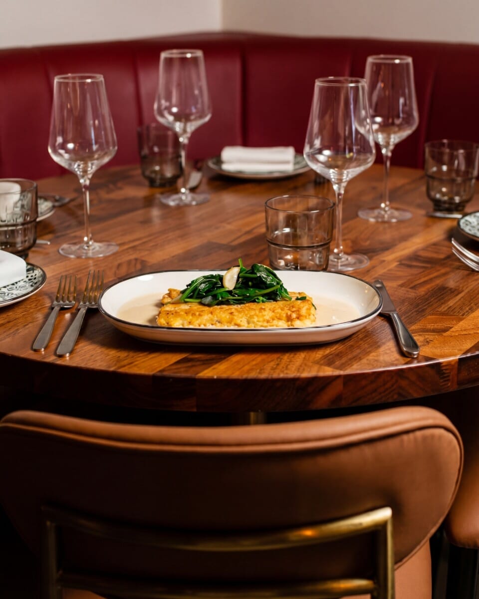 Italian food and wine served on a warm walnut restaurant table top with patterned plates, glassware, candlelight, and intimate dining atmosphere.