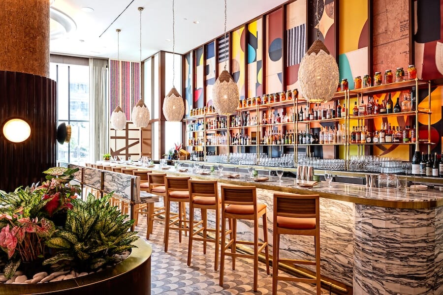 MARCUS DC bar seating featuring natural wood bar stools with Canyon Pumpkin upholstered seats and brass footrests.