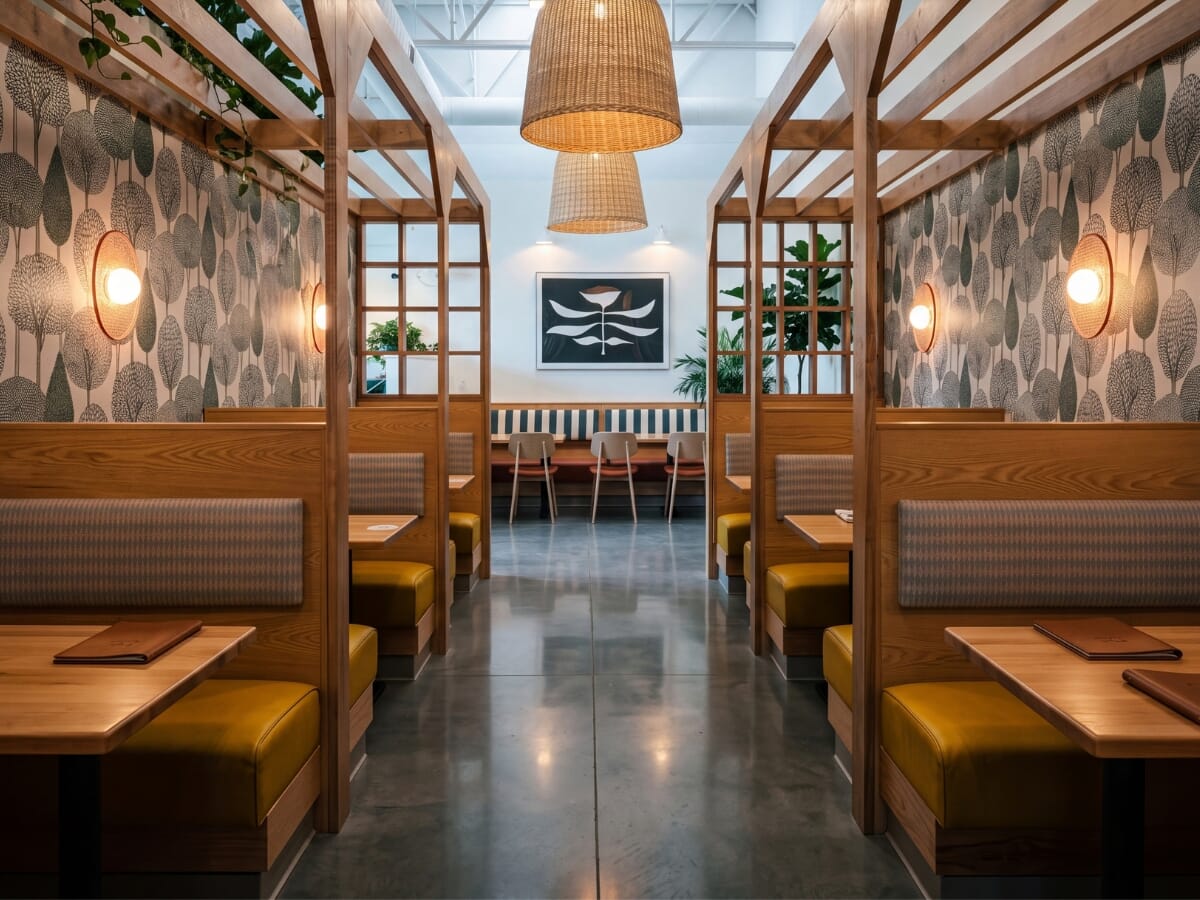 OddBird's booth corridor with exposed wood backs, rectangular upholstered pads, mustard seats, timber alcoves, and botanical wallpaper.