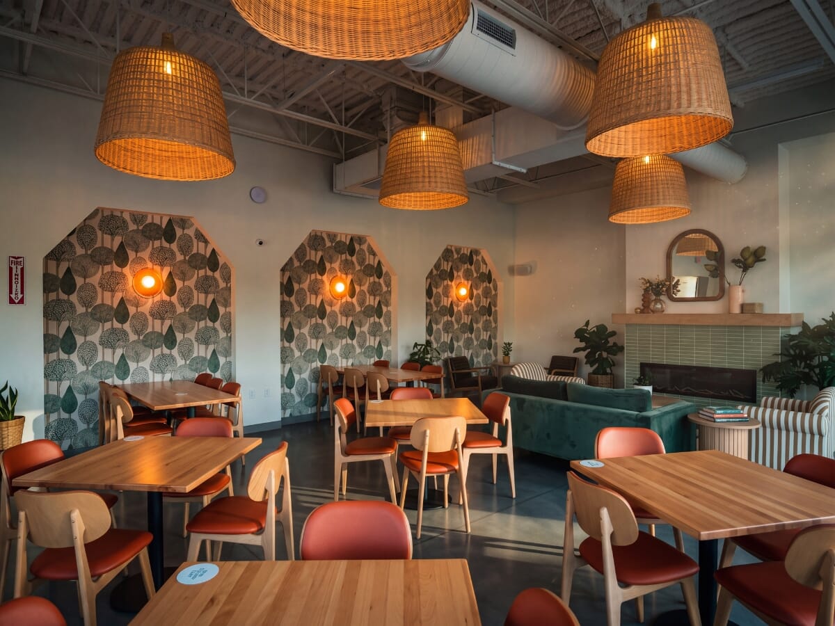OddBird Café in Akron with natural beech tables, Persimmon upholstered Lola chairs, tree-pattern wallpaper, and woven pendant lights.