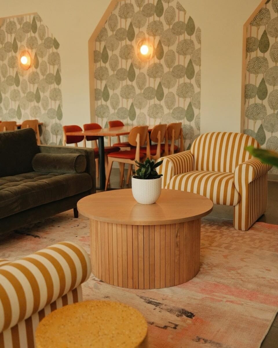 OddBird Café in Akron with natural beech tables, Persimmon upholstered Lola chairs, tree-pattern wallpaper, and woven pendant lights.