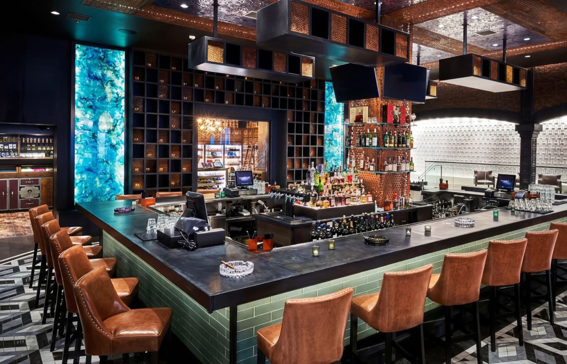 Upscale bar interior at Burn by Rocky Patel cigar lounge in Pittsburgh Pennsylvania featuring center island bar with cognac leather stools, glowing teal backlit columns, and geometric tile floor