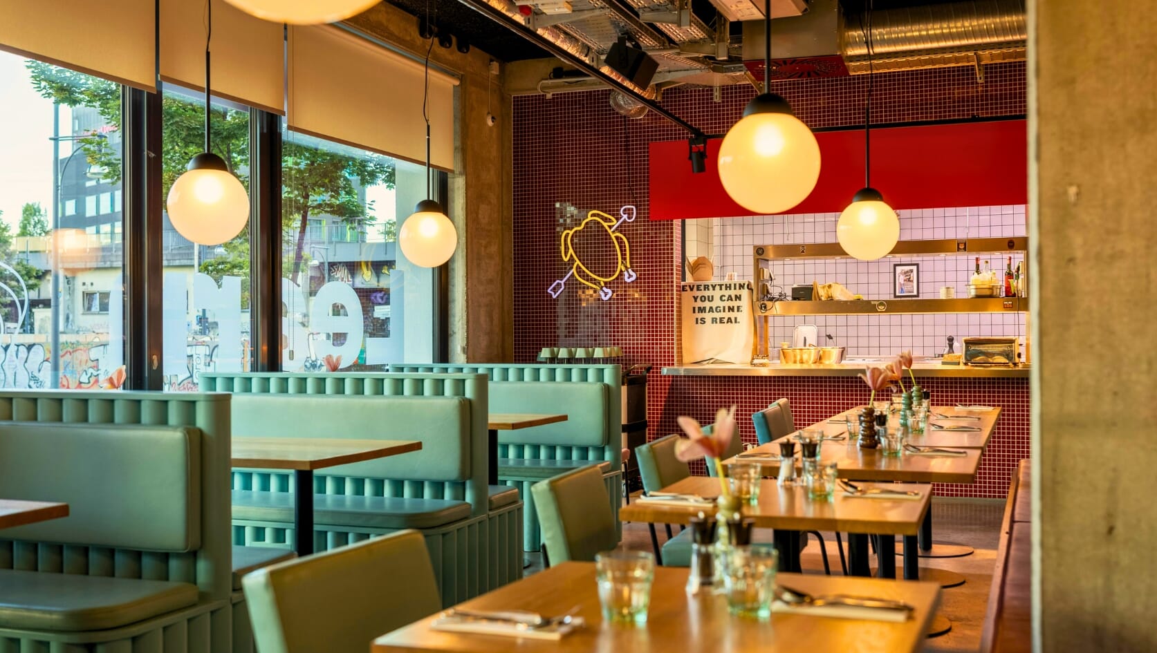 Casual dining restaurant interior — mint green booth seating along the window wall, wooden tables, and matching teal chairs in a mixed perimeter-booth and freestanding layout.
