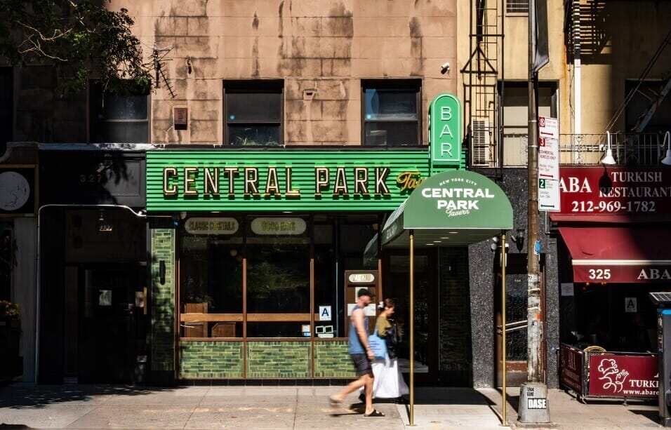 Central Park Tavern in Midtown Manhattan, featuring checkered floors, walnut tables, and a classic New York tavern bar with red-upholstered stools and brass accents.