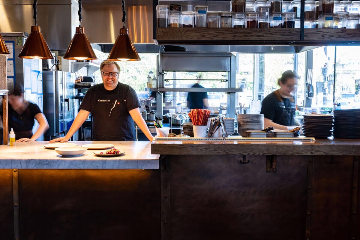 Chef Ehren Ryan at Common Lot in Millburn, NJ, preparing seasonal dishes in the restaurant’s open kitchen, emphasizing fresh, global-inspired cuisine.