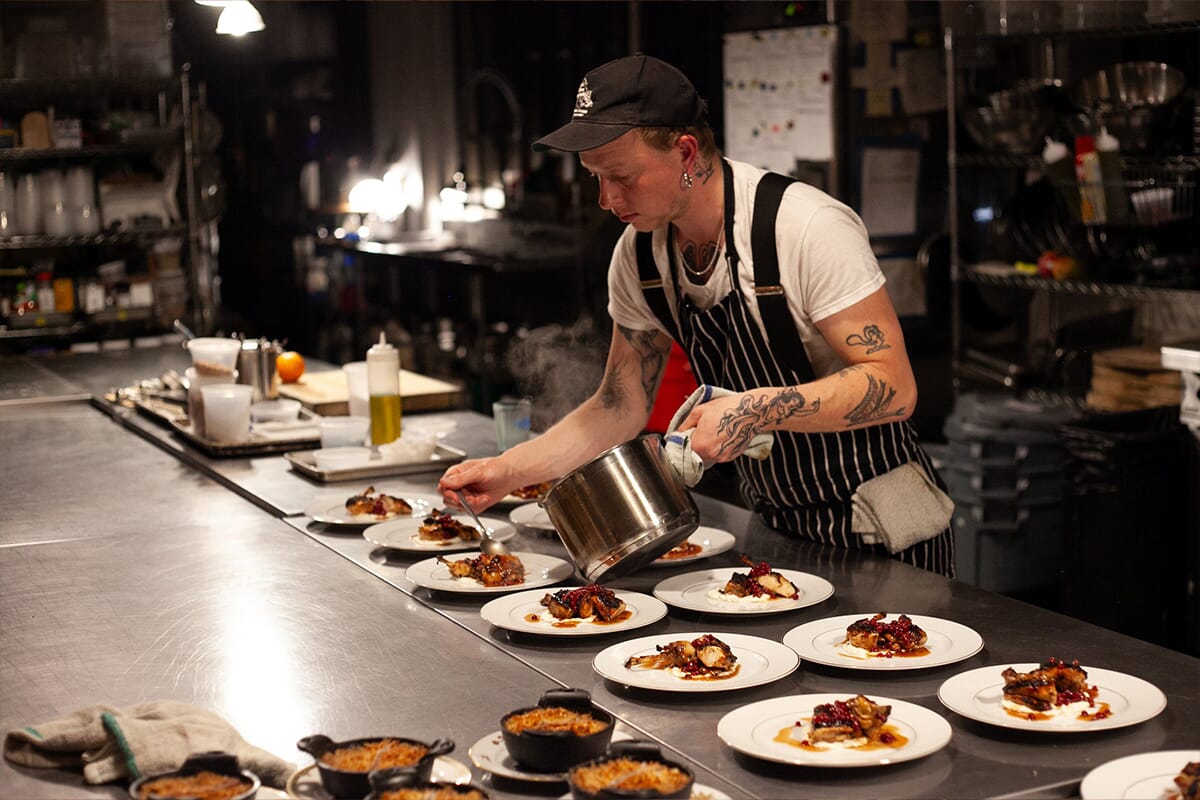 Chef Nick Forsberg prepares food on plates in a cozy kitchen, showcasing culinary skills in a warm, inviting atmosphere.