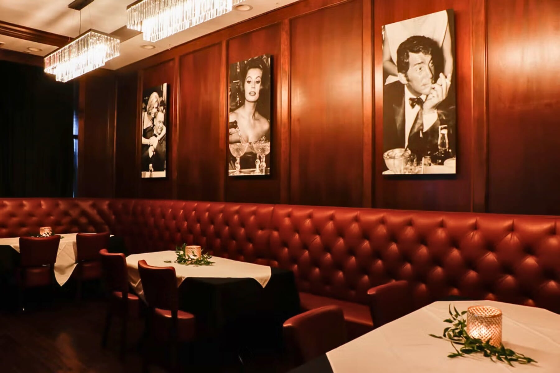 Tufted red leather banquette seating at Giancarlo's Sicilian Steakhouse — deep burgundy booths, dark wood paneling, and Italian vintage photography define a classic fine dining atmosphere