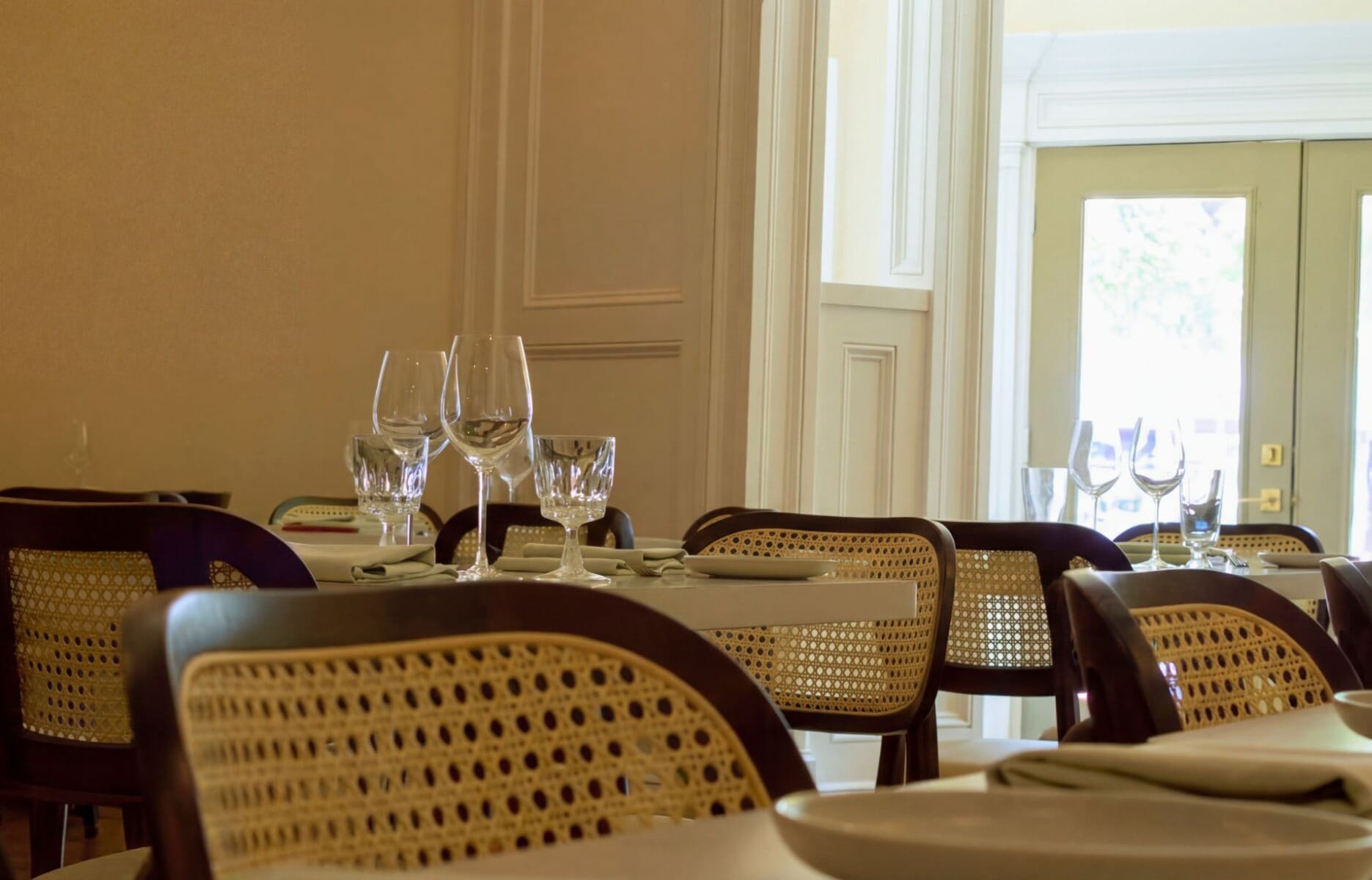 Elegant dining room interior at Isola Italian Trattoria in Westfield New Jersey featuring white linen tables, dark wood cane-back chairs, and French doors with natural light