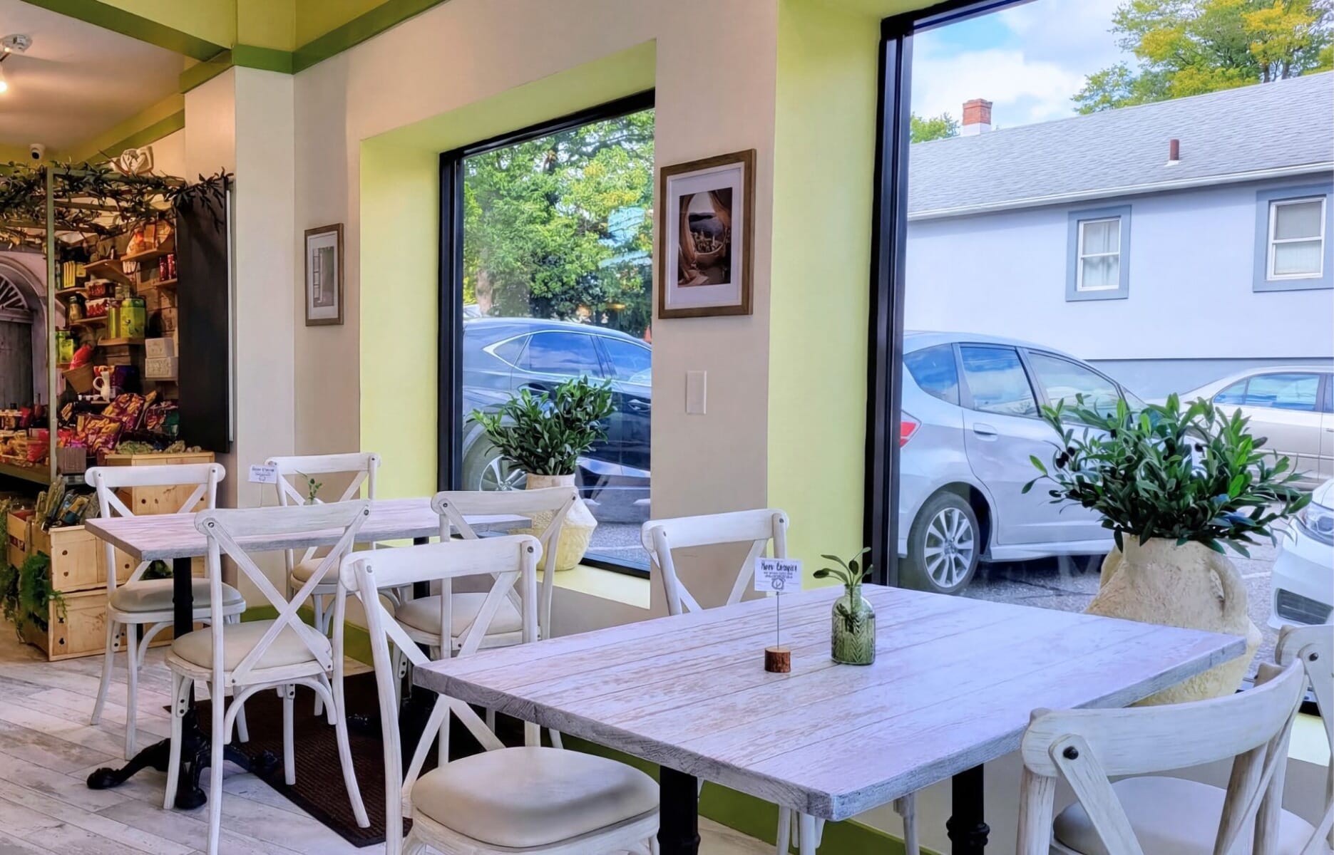 Bright casual dining room at Just Greek restaurant in Caldwell New Jersey featuring whitewashed wood table tops, white cross-back chairs, lime green accents, and large picture windows