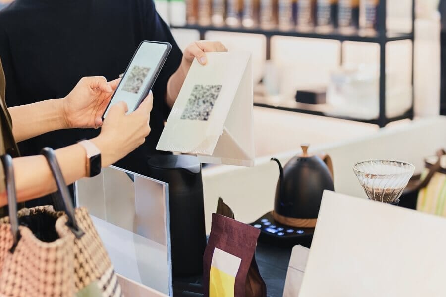 Customer scanning a QR code at a coffee shop checkout to access digital loyalty rewards, showcasing modern incentive programs for boosting restaurant customer retention.