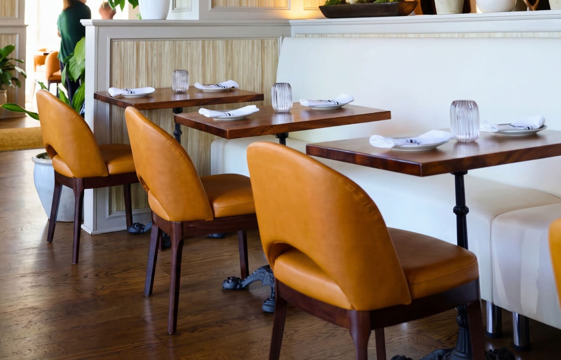 Dining room detail at Meli European Taverna in Easton Pennsylvania featuring cognac leather barrel chairs, warm walnut table tops, white upholstered banquette, and hardwood floors