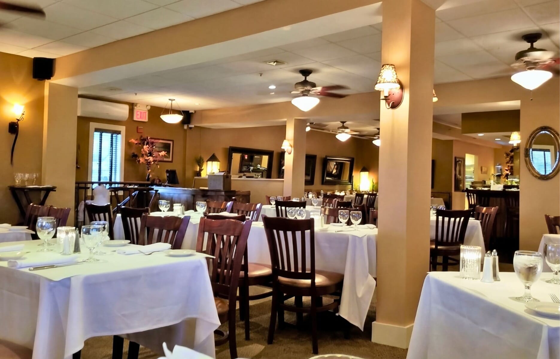 Spacious dining room interior at Moonstruck restaurant in Asbury Park New Jersey featuring white linen tables, dark wood chairs, warm wall sconces, and ceiling fans
