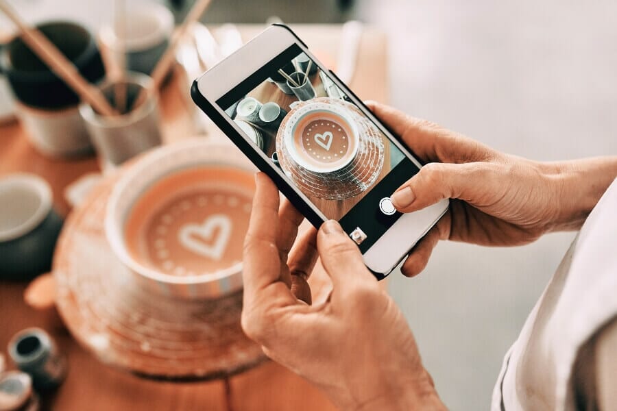 Person taking a photo of a latte with heart art for social media marketing, highlighting restaurant storytelling and customer engagement during economic uncertainty.