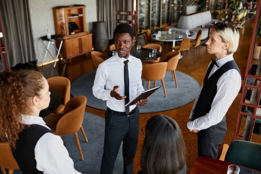 Restaurant manager leading a team huddle with staff before service, discussing training goals and role flexibility to improve efficiency and team performance.