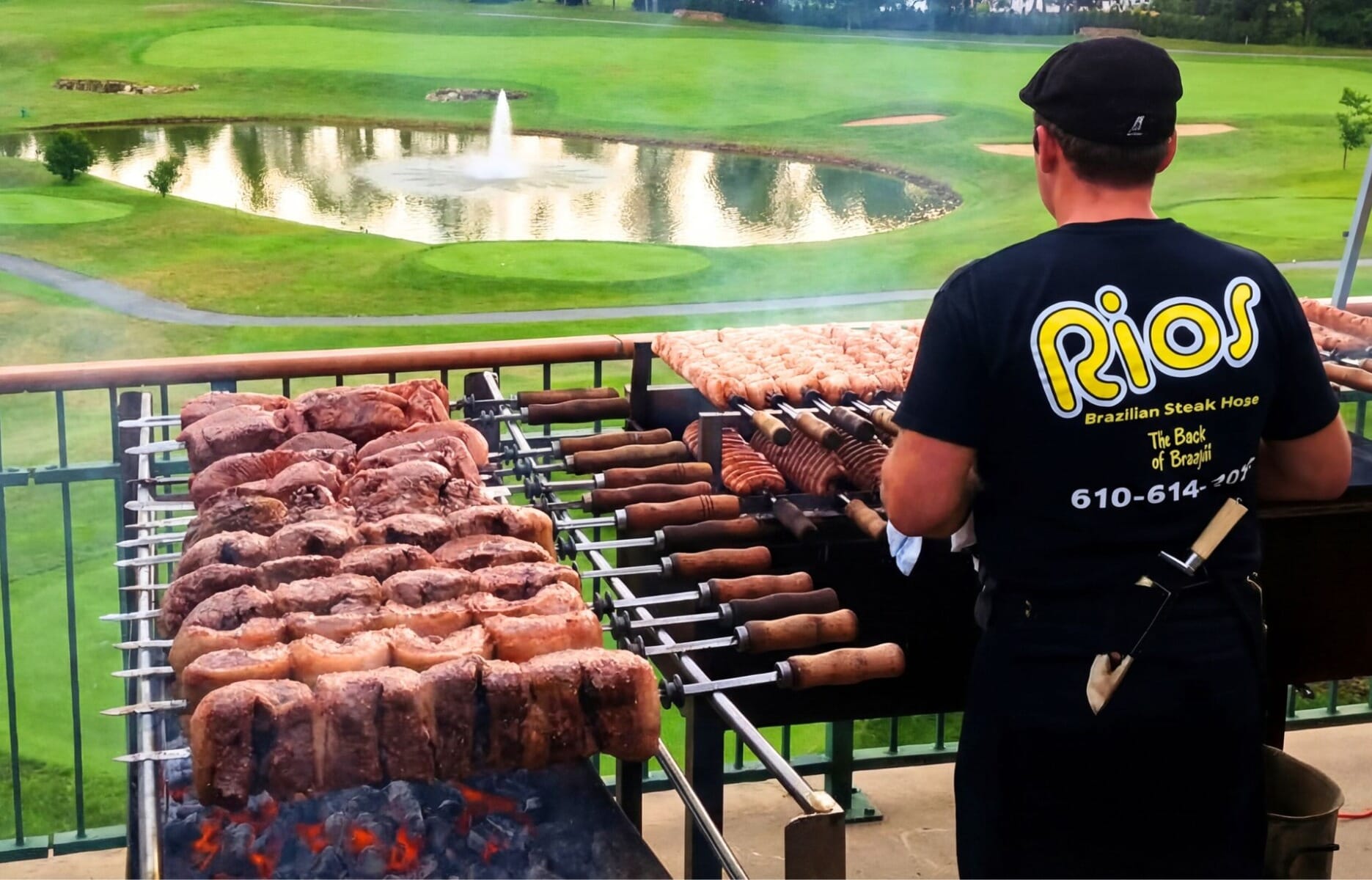 Rios Brazilian Steakhouse chef grilling skewers of meat over open coals on an outdoor terrace overlooking a golf course and pond in Easton Pennsylvania