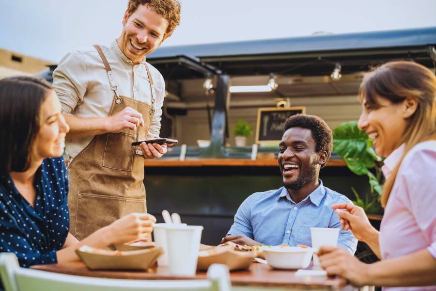 Server taking orders from smiling group of diverse customers in a casual outdoor restaurant patio setting