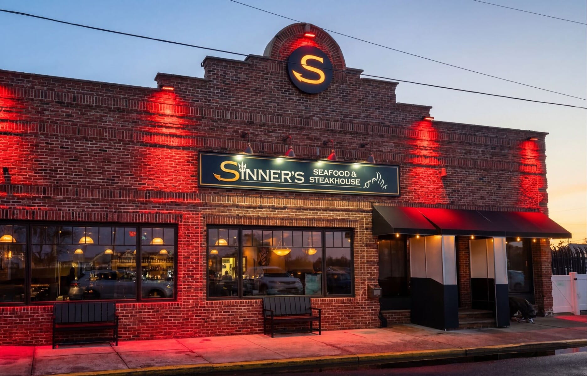 Exterior of Sinner's Seafood and Steakhouse in Point Pleasant Beach New Jersey featuring red brick facade with dramatic red uplighting and illuminated signage at dusk