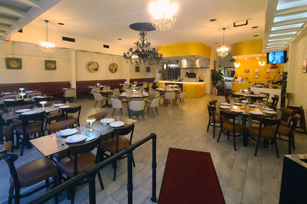 A warm restaurant interior featuring tables, chairs, and an elegant chandelier, embodying a blend of Albanian and Mediterranean cuisine.