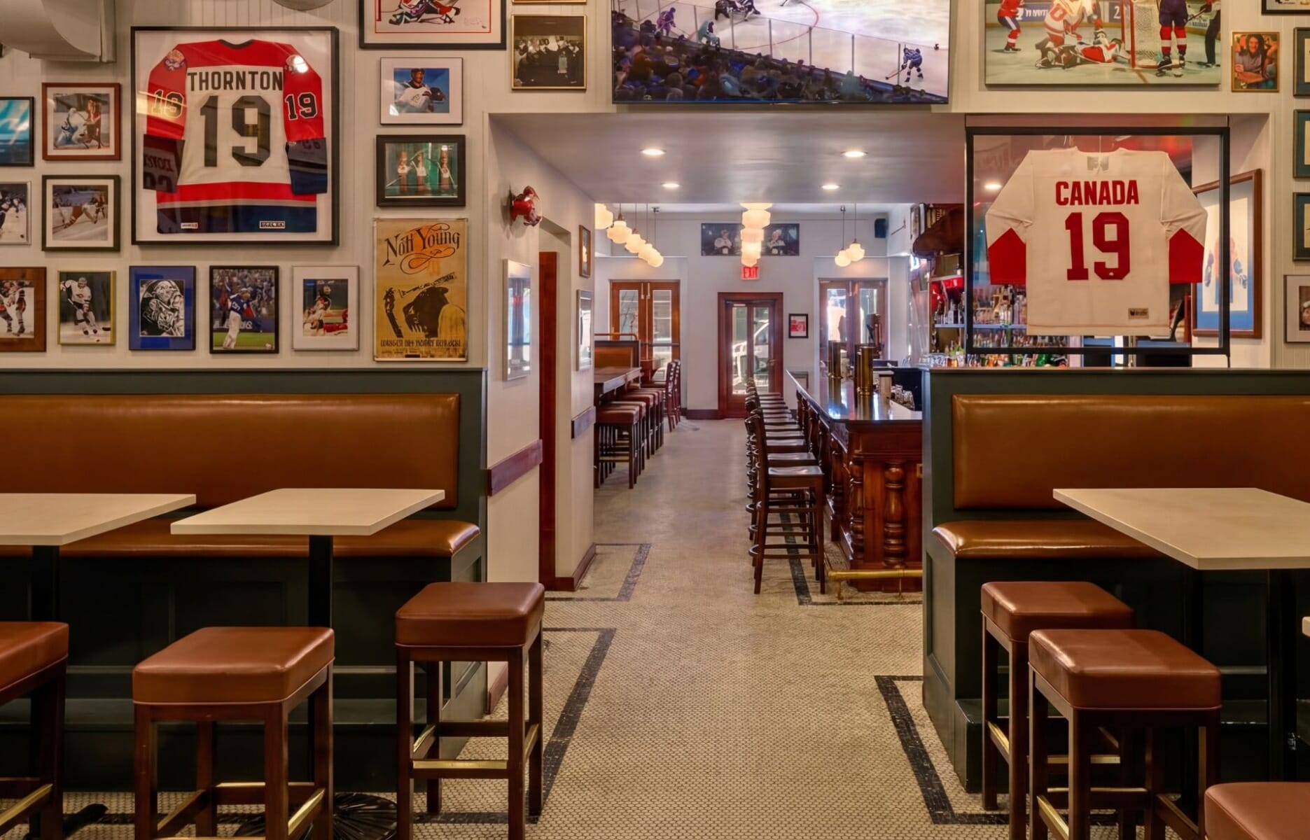 Interior of The Canuck NYC sports bar in New York featuring cognac leather booths, white marble tables, and walls lined with framed hockey jerseys and Canadian sports memorabilia