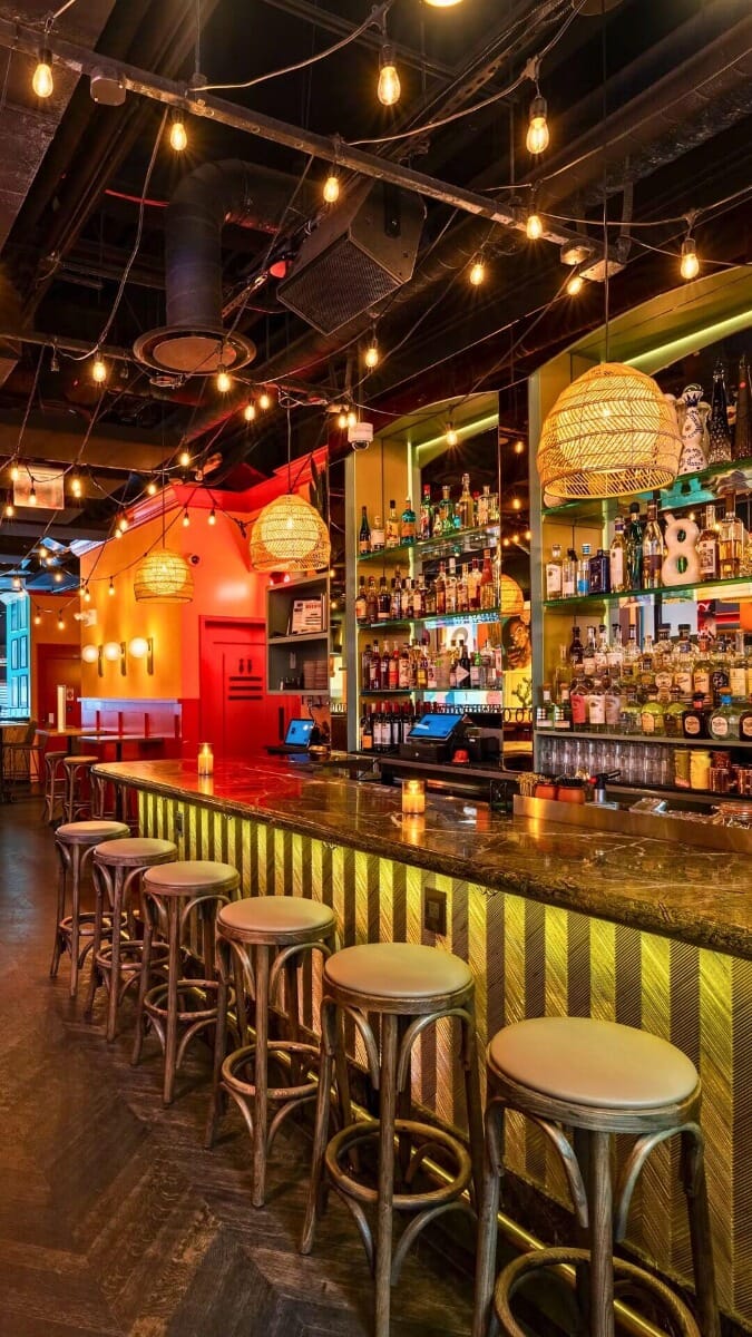 Main bar inside Vida Verde Tequila Bar in Manhattan featuring pendant lights, wooden stools, and tropical-inspired wall décor