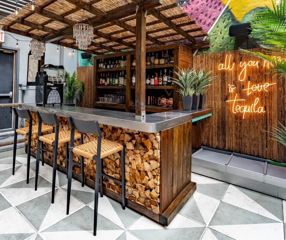 Outdoor bar at Vida Verde Tequila Bar in New York City with wood accents, tropical décor, and neon sign reading ‘All You Need Is Love & Tequila’