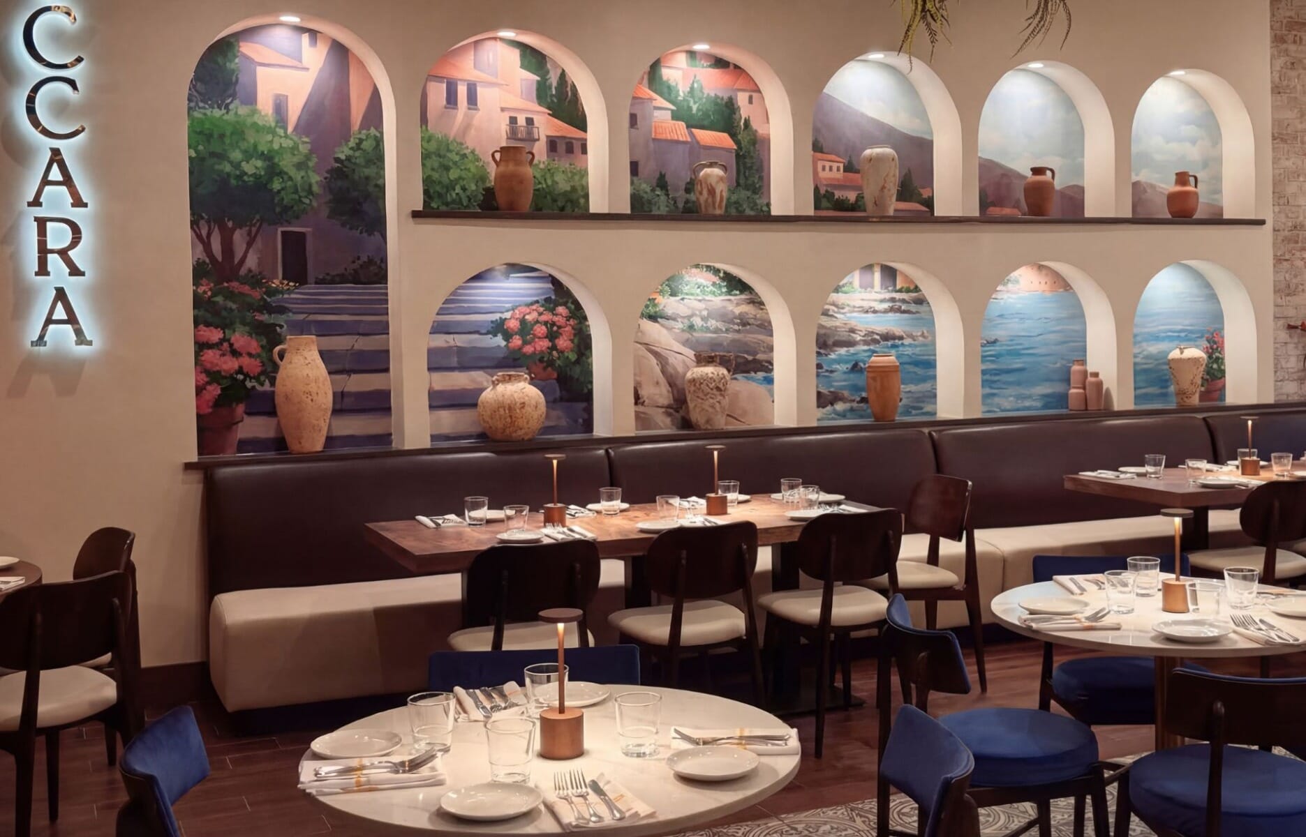 Dining room interior at Villaggio Iccara in Yardville New Jersey featuring arched wall niches with Italian coastal murals, terra cotta urns, leather banquette, and navy velvet chairs