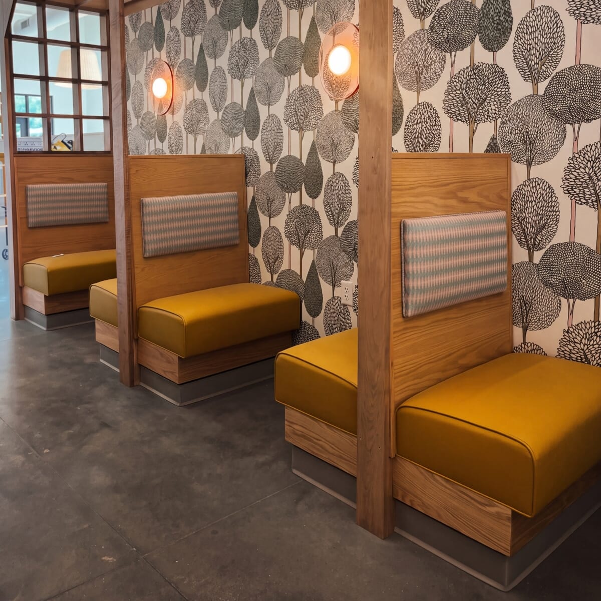 Close view of OddBird's custom booth backs with rectangular COM-upholstered pads mounted on exposed wood above mustard seats.