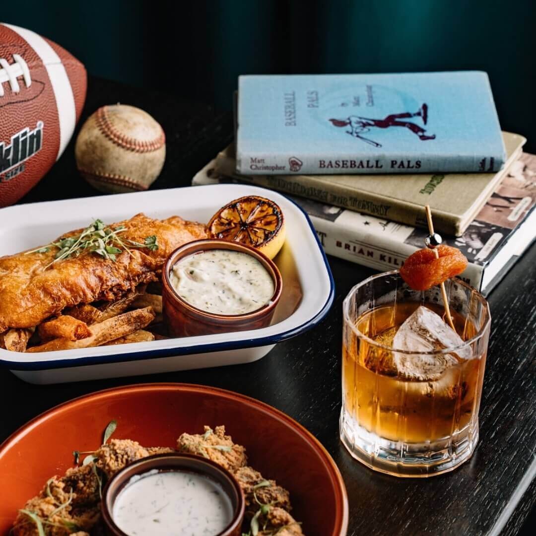 Classic fish and chips with craft cocktail and sports decor at Central Park Tavern in Midtown NYC, highlighting casual tavern dining atmosphere.
