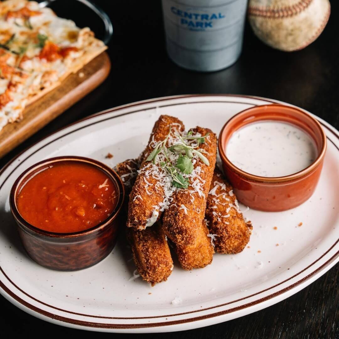 Crispy mozzarella sticks served with marinara and ranch dipping sauces at Central Park Tavern NYC, set on dark walnut restaurant tables.