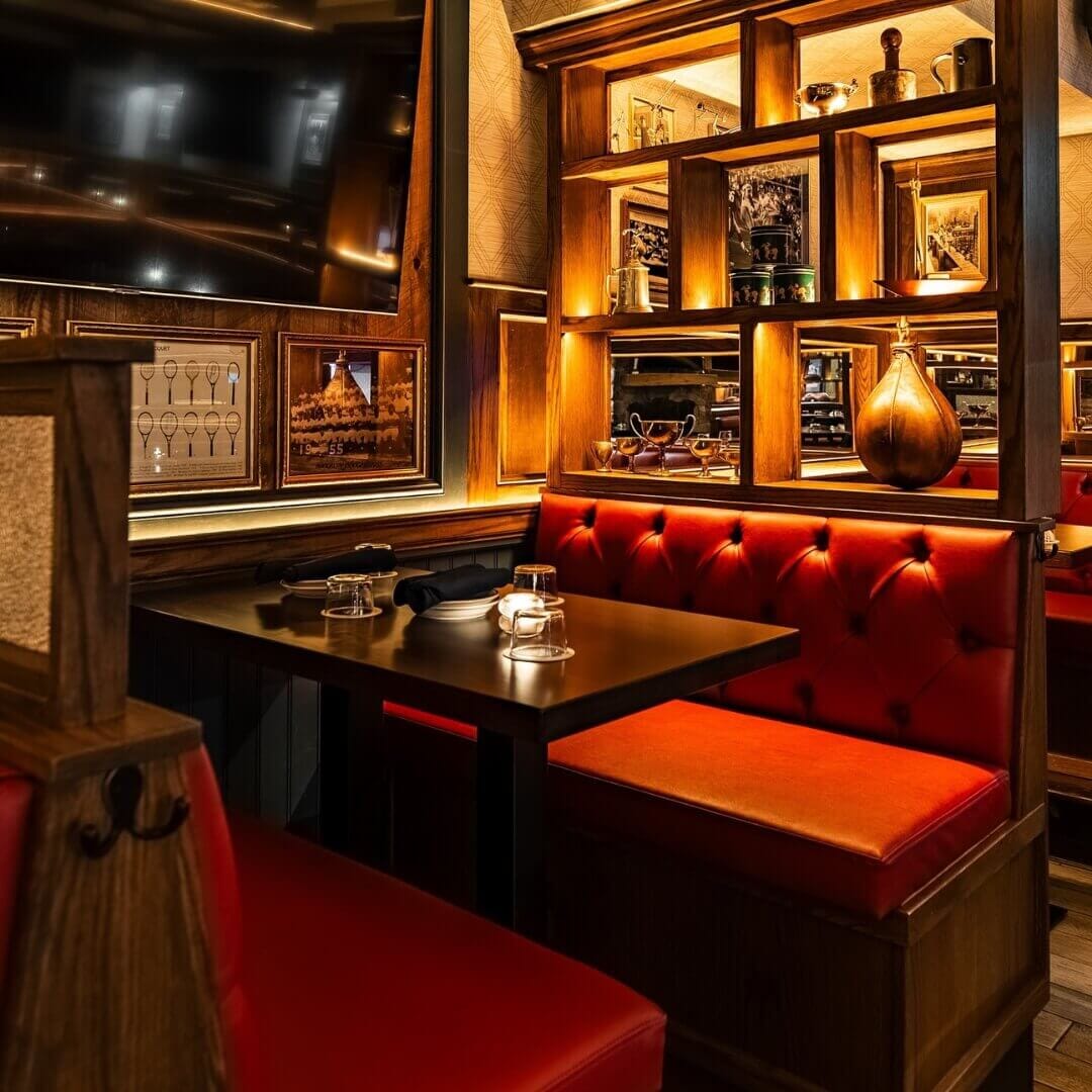 Restaurant booth seating at Central Park Tavern New York with tufted red upholstery, walnut tables, and decorative shelving for a classic tavern look.