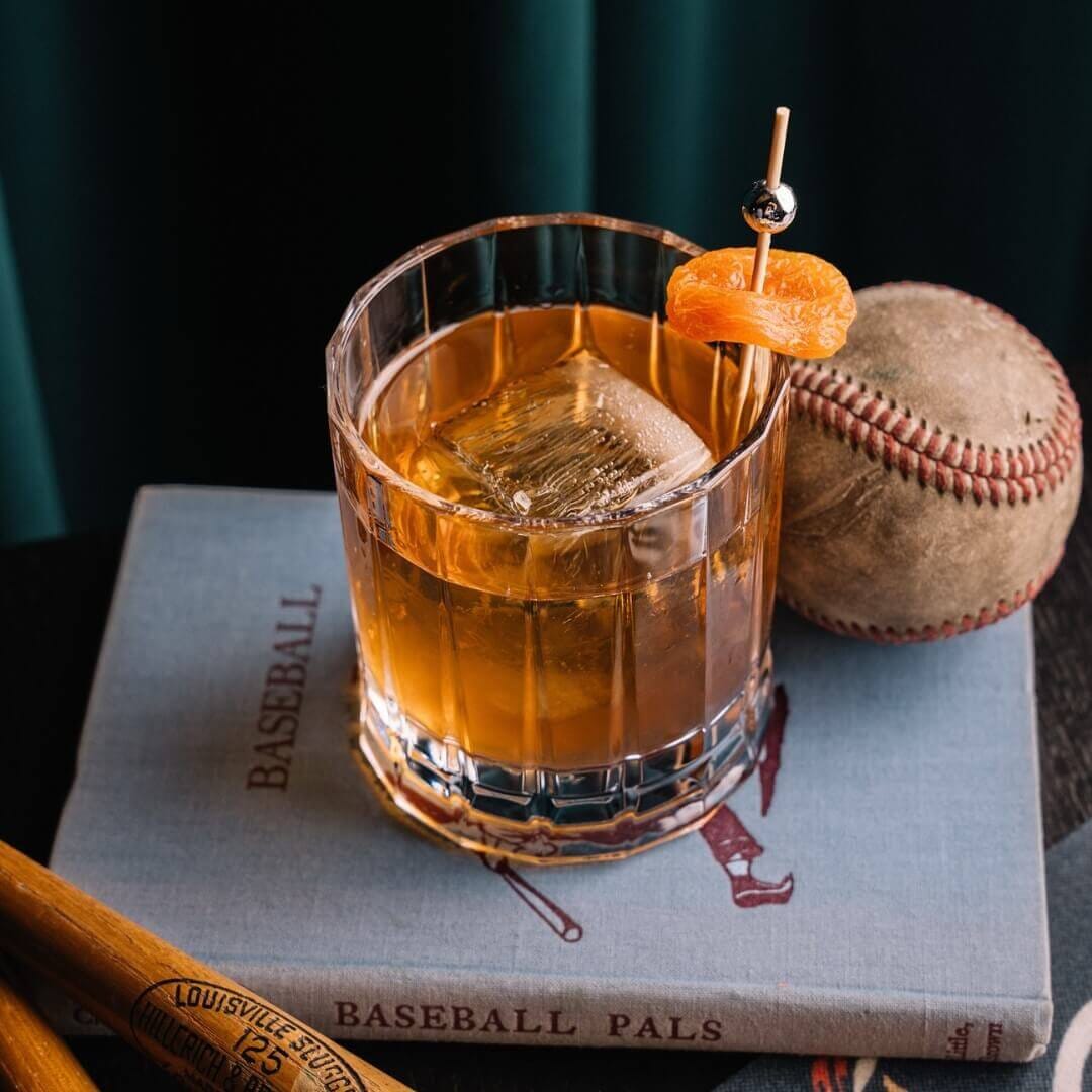 Signature Old Fashioned cocktail served at Central Park Tavern NYC, styled with baseball memorabilia to reflect the tavern’s vintage sports theme.