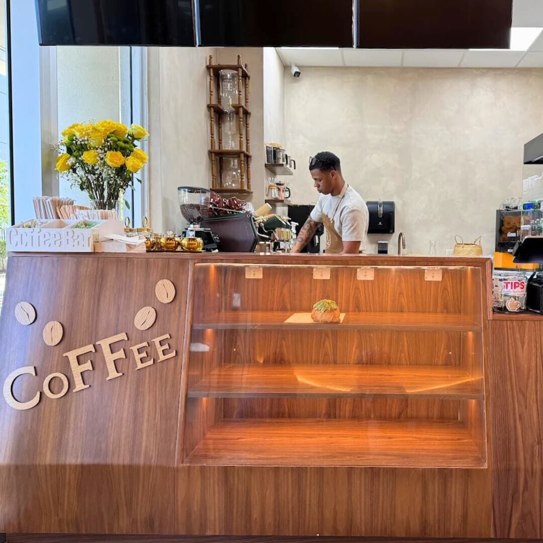 Barista preparing coffee behind STL Cafe’s walnut-paneled coffee counter with floral decor