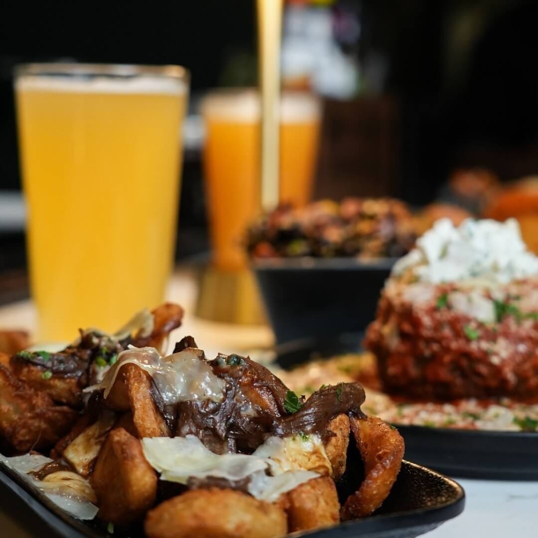 Short-rib poutine with melted cheese beside hazy beer and brass lamp at Strickland’s Steakhouse bar.