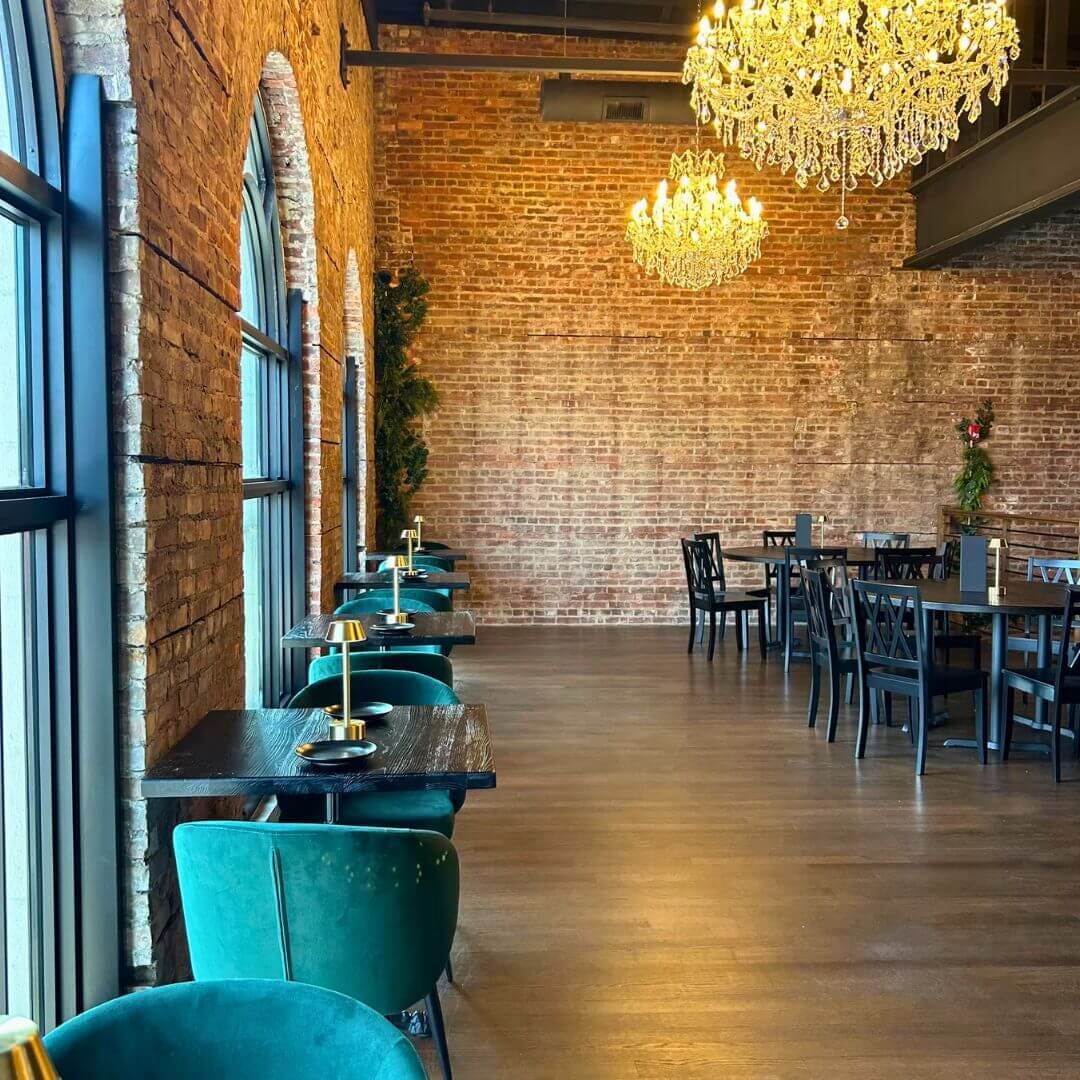 Exposed-brick dining room with crystal chandeliers, green velvet chairs and black plank tables at Strickland’s Steakhouse.