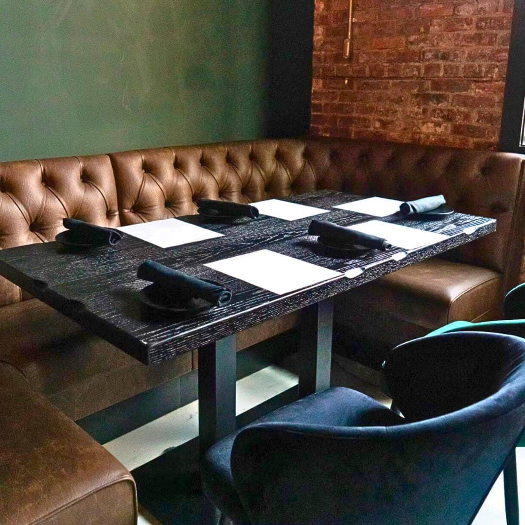 Tufted leather banquette and rustic black oak plank table with industrial base at Strickland’s Steakhouse.