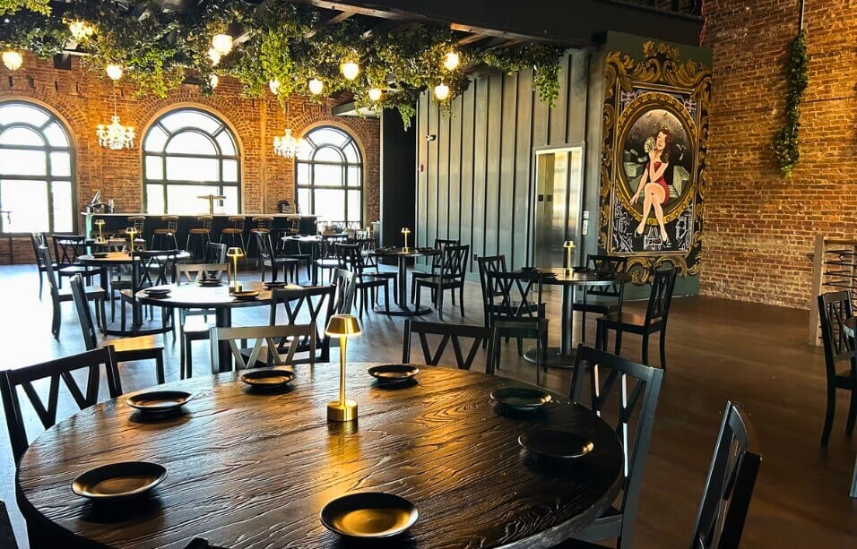 Strickland’s Steakhouse dining room with rustic black oak table tops, brick walls and plush custom chairs.