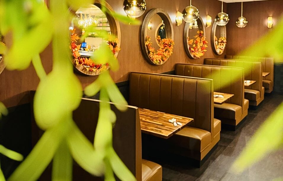 Row of chestnut channel-back booths at Thai Season Carmel with walnut tables, round mirrors, globe pendants and fall wreaths.