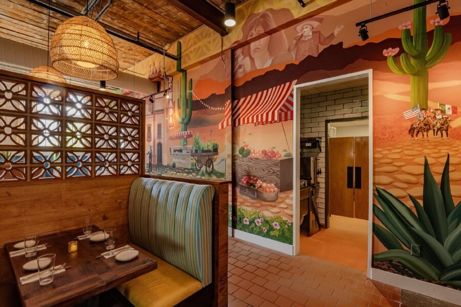 De Nada Birmingham interior with colorful Mexican-inspired desert mural, custom striped restaurant booths, terracotta tile floor, woven pendant lights, exposed ductwork, and decorative breeze-block partitions.