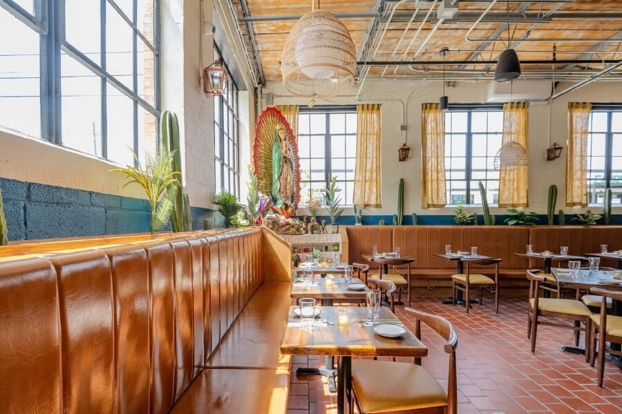 De Nada Birmingham interior with colorful Mexican-inspired desert mural, custom striped restaurant booths, terracotta tile floor, woven pendant lights, exposed ductwork, and decorative breeze-block partitions.
