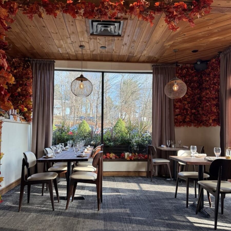 Bora Restaurant dining area with floral ceiling installation, wood tables, cream seating, and fireplace feature wall.