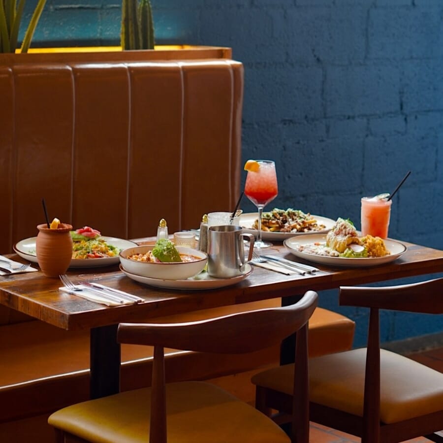 De Nada Birmingham cantina-style bar with antique walnut commercial bar stools, tan and rust upholstery, patterned tile, arched niches, hanging plants, and woven pendant lighting.