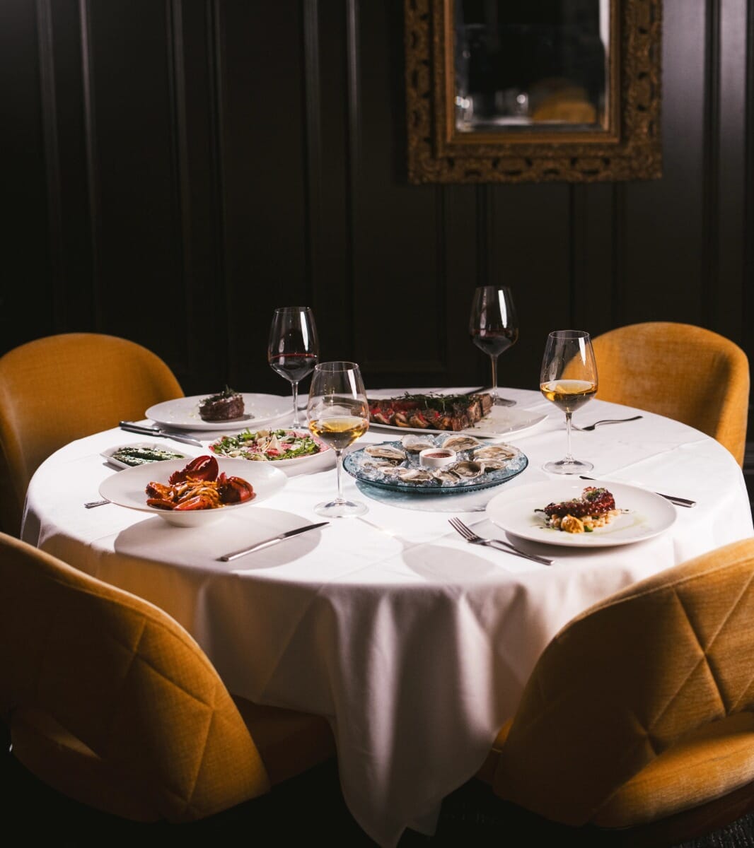Communal dining table with upholstered chairs and chandelier lighting.